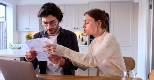 Worried Couple at Home Looking at Laptop Holding Energy Bill