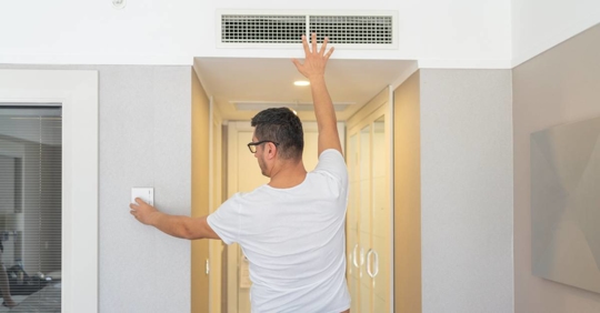 Man Adjusts The Room Temperature From The Air Conditioning Panel