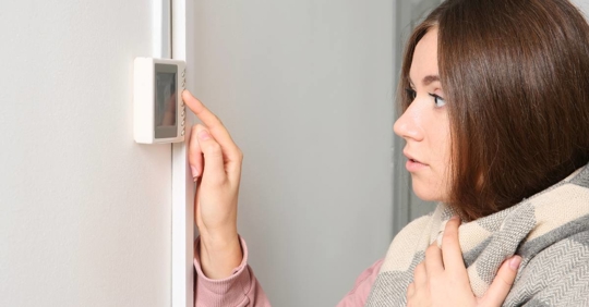 person adjusting a wall-mounted thermostat to control indoor temperature